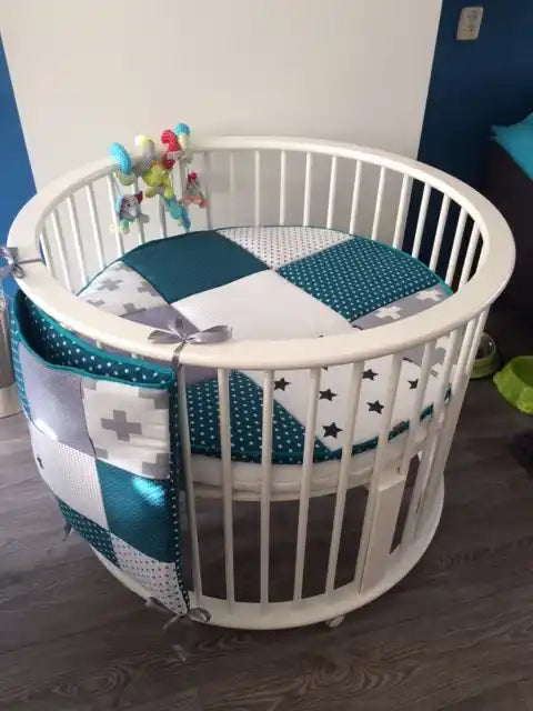 Witte ovale babywieg met turquoise en grijze beddengoed met patroon.